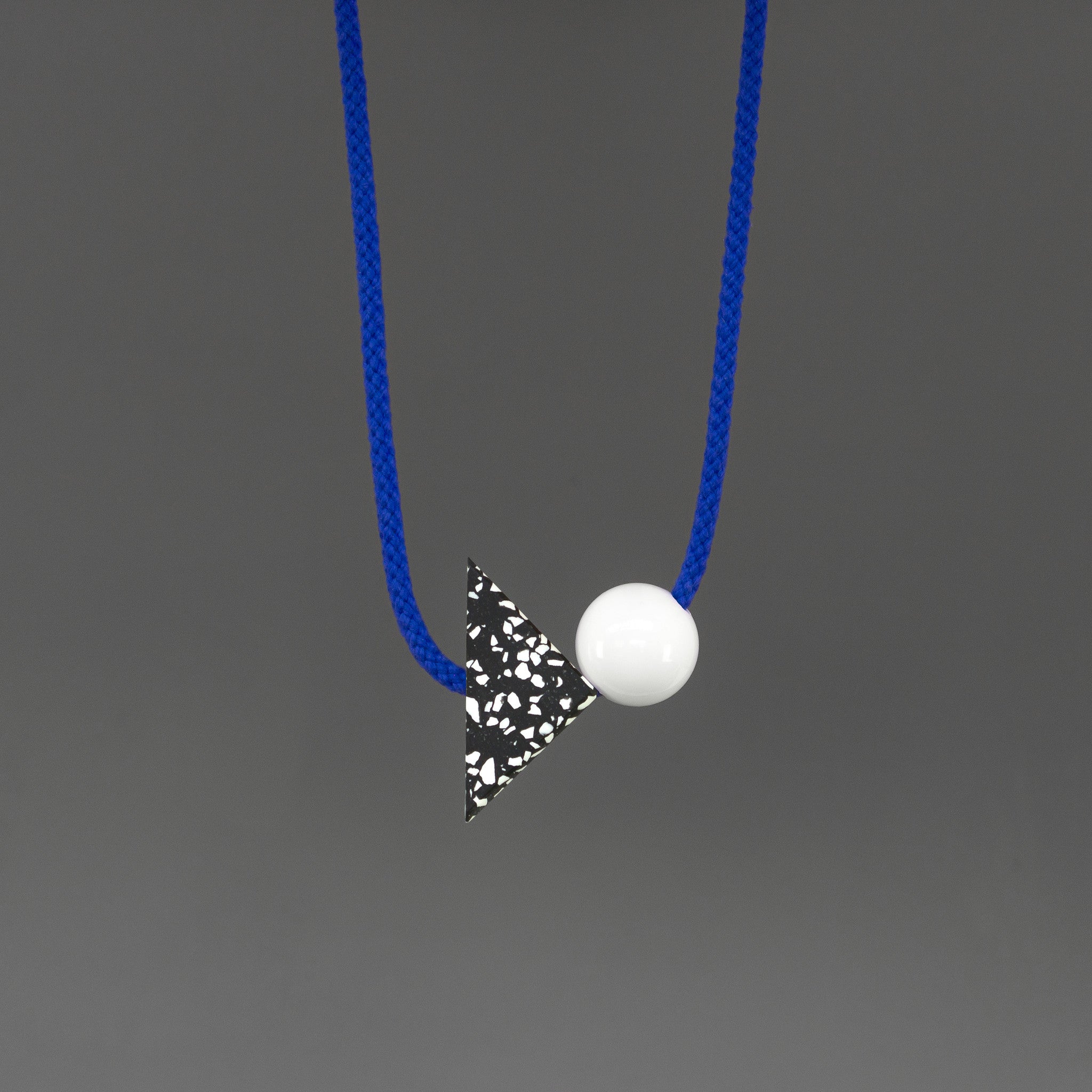 The Ilya necklace is a bright and bold statement. Stepping away from our signature black cord, Ilya's bright blue cord offers something different and looks great against a variety of tops. Illya is composed of 2 main parts - a black triangle with white speckles (70mm x 50mm) and a white resin ball (30mm). 