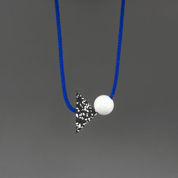 The Ilya necklace is a bright and bold statement. Stepping away from our signature black cord, Ilya's bright blue cord offers something different and looks great against a variety of tops. Illya is composed of 2 main parts - a black triangle with white speckles (70mm x 50mm) and a white resin ball (30mm). 