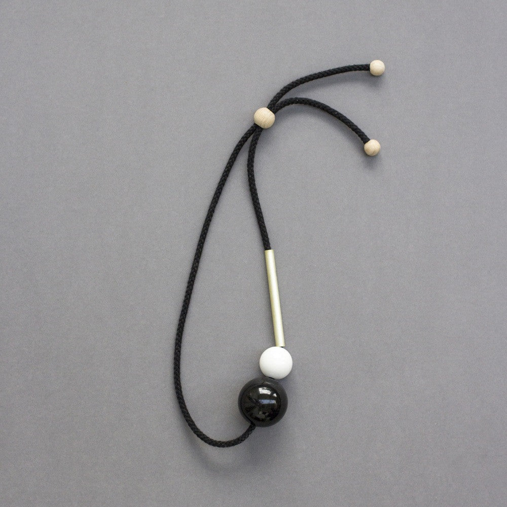 Minimal necklace design by London design studio One We Made Earlier. Black and white resin balls and a brass tube. Necklace is fully adjustable. Contemporary design.