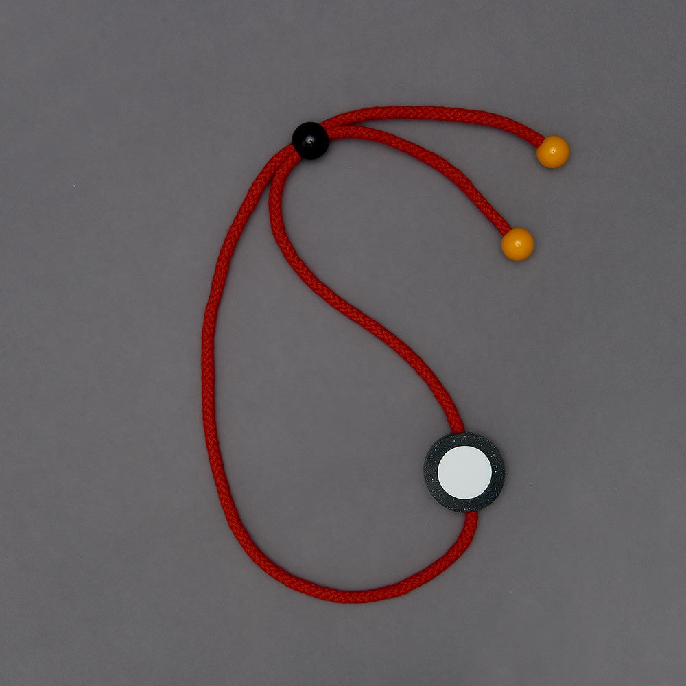 The Ed necklace is part of the collection we launched with Transport For London at Clerkenwell Design Week 2017.Bright and striking necklace. Bright red rope. Small yellow balls on the end of each rope. (15mm)Black speckled resin circle 40mm diameter x 10mm White resin circle which sits inside, 30mm x 10mm