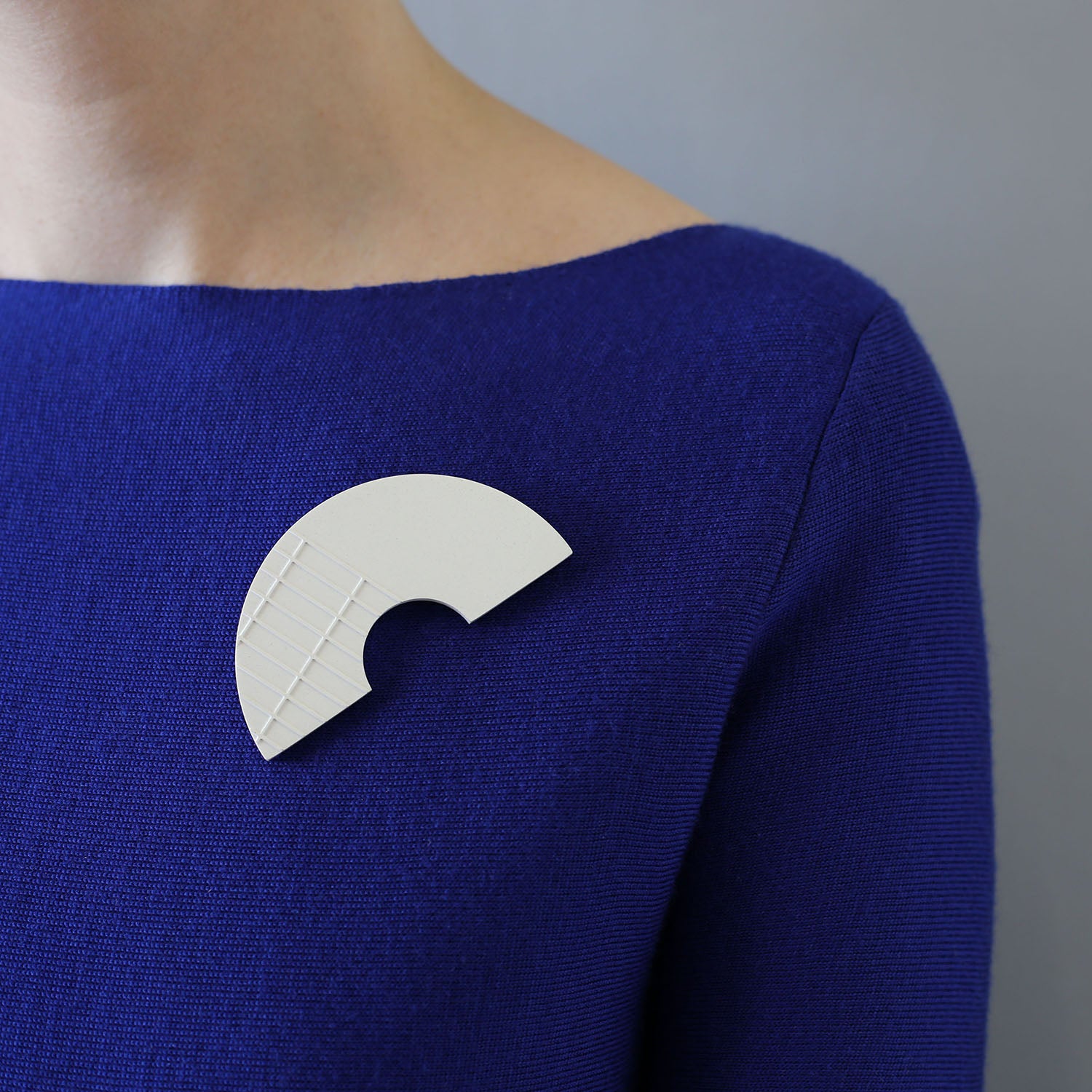 Model wearing handcast brooch inspired by the brutalist architecture of London's Barbican centre. Gil has a raised grid pattern on part of the surface. Each brooch is cast by hand in our south London studio and comes in branded gift box. (8cm x 4cm)