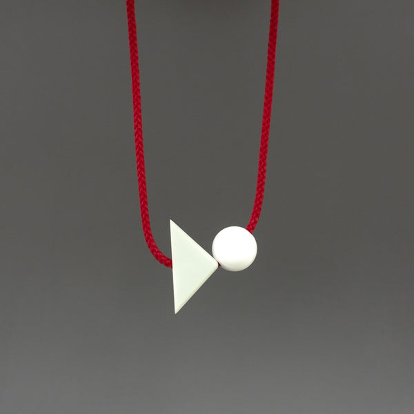 Bold, simple and playful necklace. Looks great on a simple top. Pale green corian triangle on a bright red cord with a resin ball. Geometric contemporary necklace.