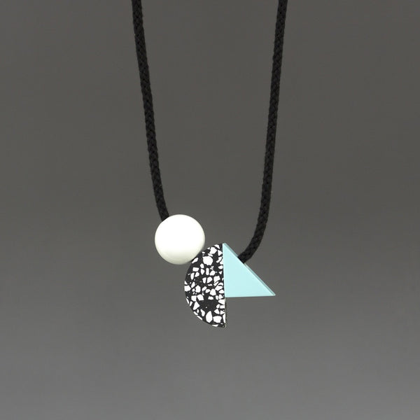 Bold and striking necklace composed of 3 geometric shapes on black cord. A handcast black and white curve sits between a shiny white ball and pale blue resin triangle. Handmade in London studio.