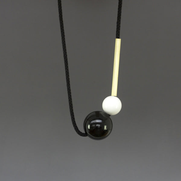 Minimal necklace design by London design studio One We Made Earlier. Black and white resin balls and a brass tube. Necklace is fully adjustable. Contemporary design.