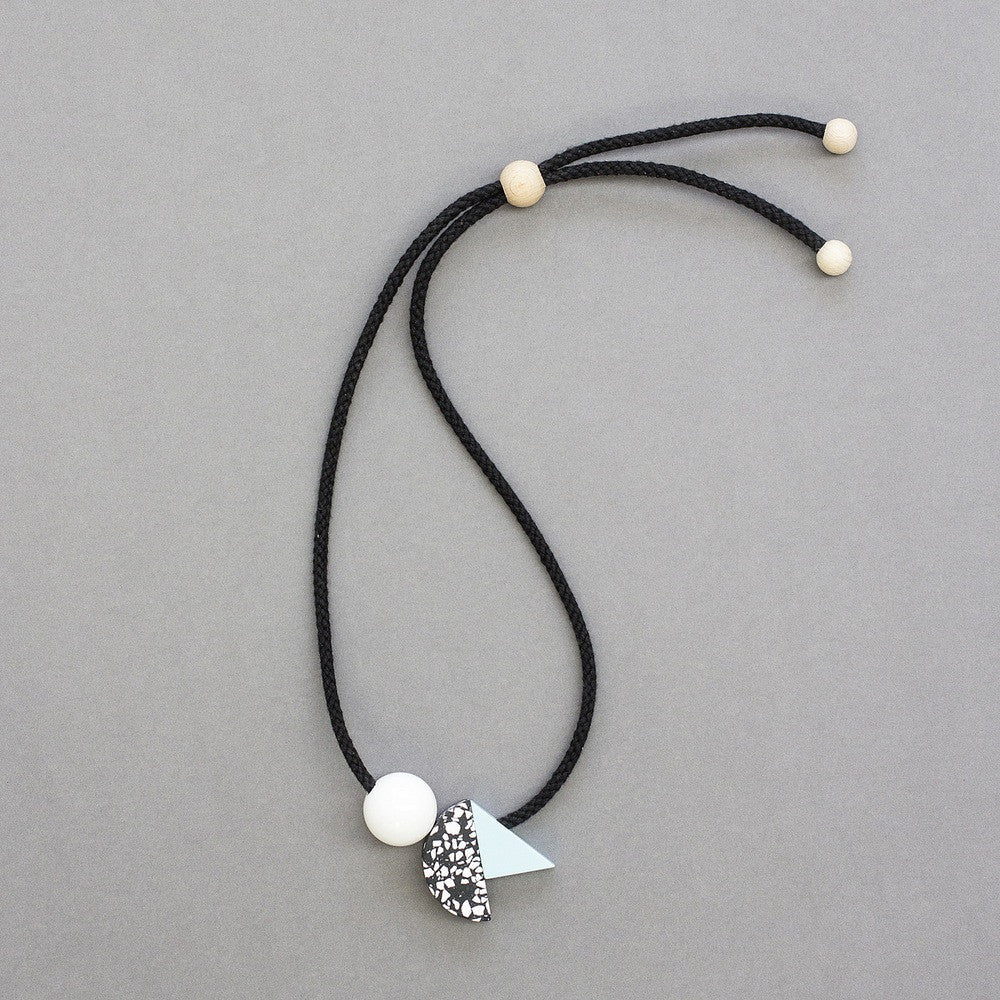 Bold and striking necklace composed of 3 geometric shapes on black cord. A handcast black and white curve sits between a shiny white ball and pale blue resin triangle. Handmade in London studio.