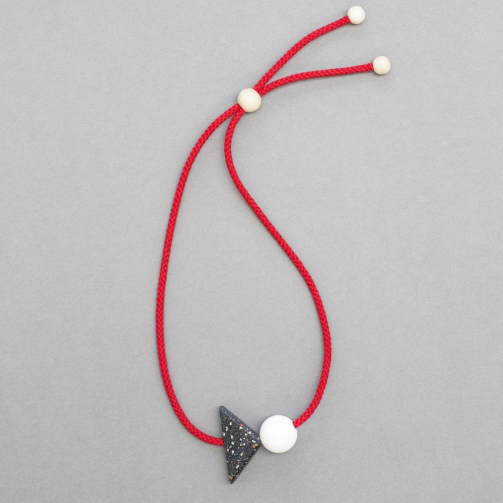 Bold and striking geometric necklace composed of resin parts on bright red cord. Resin triangle is black with little coloured speckles. Measures 70 x 50mm  Necklace can be worn high at neck length or as a longer pendant due to adjustable cord.Full drop is 45cm Handmade in our London studio.