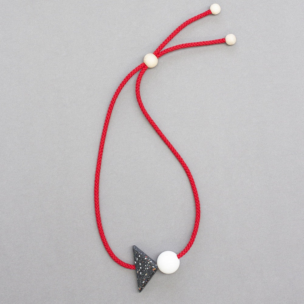 Bold and striking geometric necklace composed of resin parts on bright red cord. Resin triangle is black with little coloured speckles. Measures 70 x 50mm  Necklace can be worn high at neck length or as a longer pendant due to adjustable cord.Full drop is 45cm Handmade in our London studio.