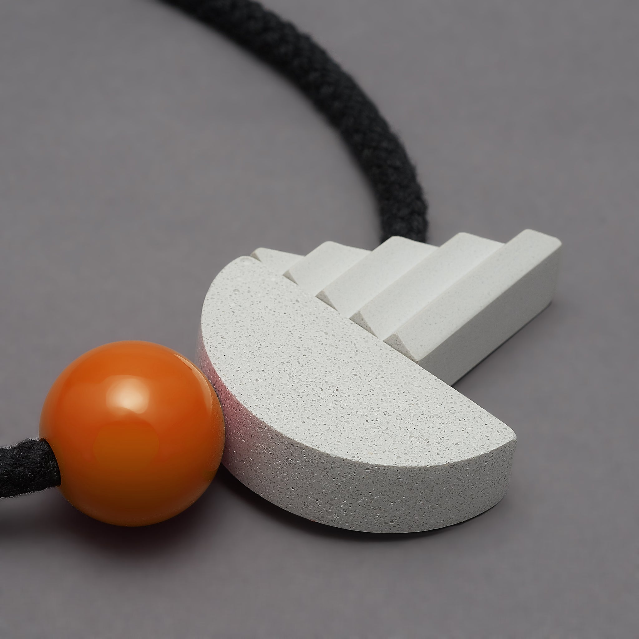 The pop necklace is composed of 2 handcast shapes. A lovely concrete-effect curve measuring 50mm x 25mm which sits beside a cast ridged triangle which measures 30mm x 45mm. The bright orange ball (25mm) offers a pop of colour beside the understated concrete resin shapes.